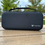 Closed Vaultica PlayStation Portal hard shell case sitting on an outdoor bench, displaying the durable textured EVA exterior, reinforced carrying handle, and Vaultica logo.